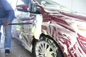 A car being washed with a broom, showing the improper preparation methods often used by tint shops offering cheap paint protection.