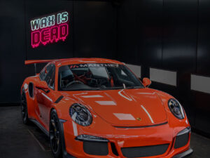 Red Porsche in a studio with Wax is Dead ceramic coating Perth neon sign in the background.